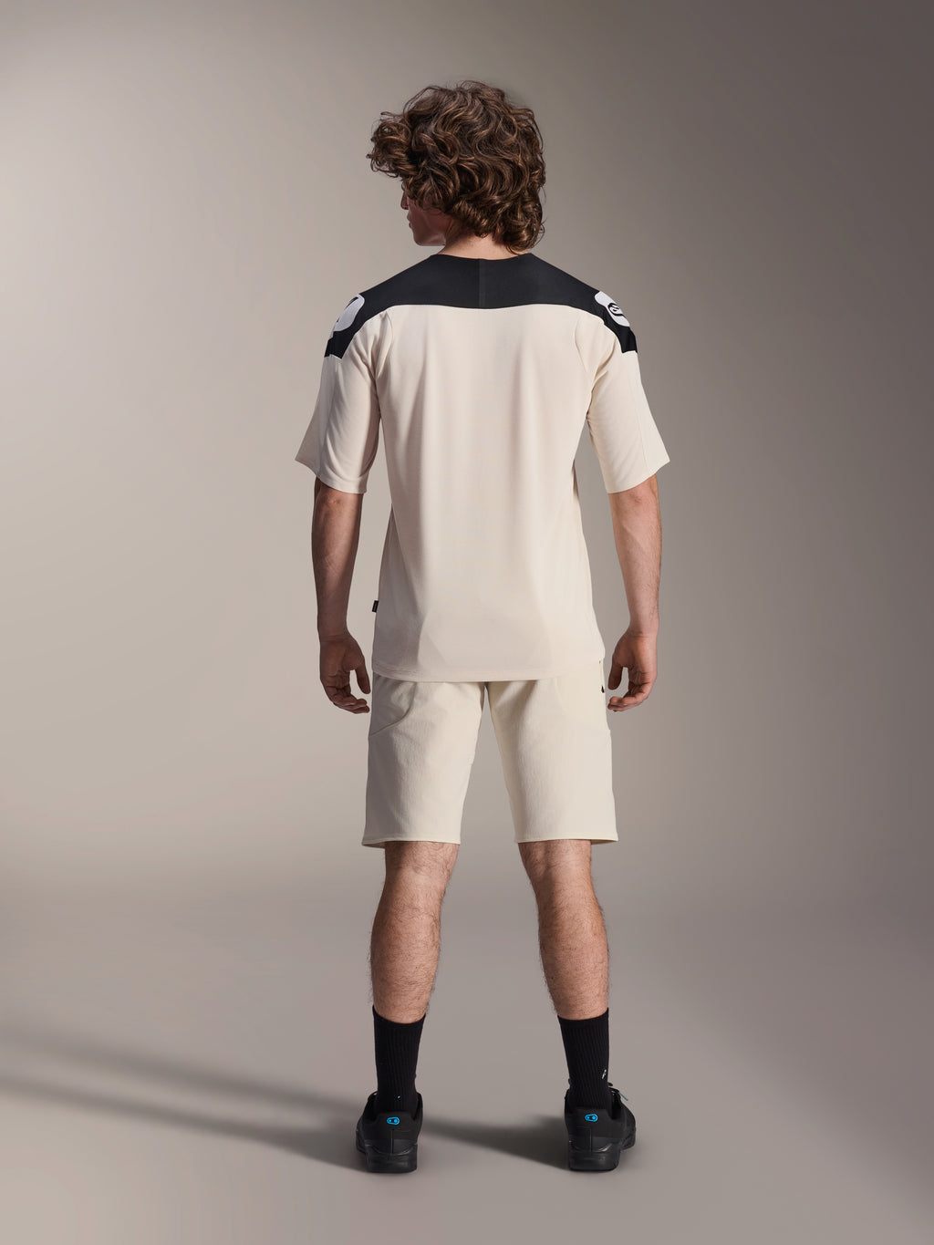 Pantaloncini Alpinestars A-Aria Elite e maglia A-Aria Polartec Elite SS, colore Ecru con pannelli neri sulle spalle, vista posteriore di un modello con abbigliamento tecnico da mountain bike, abbinato a calze e scarpe nere