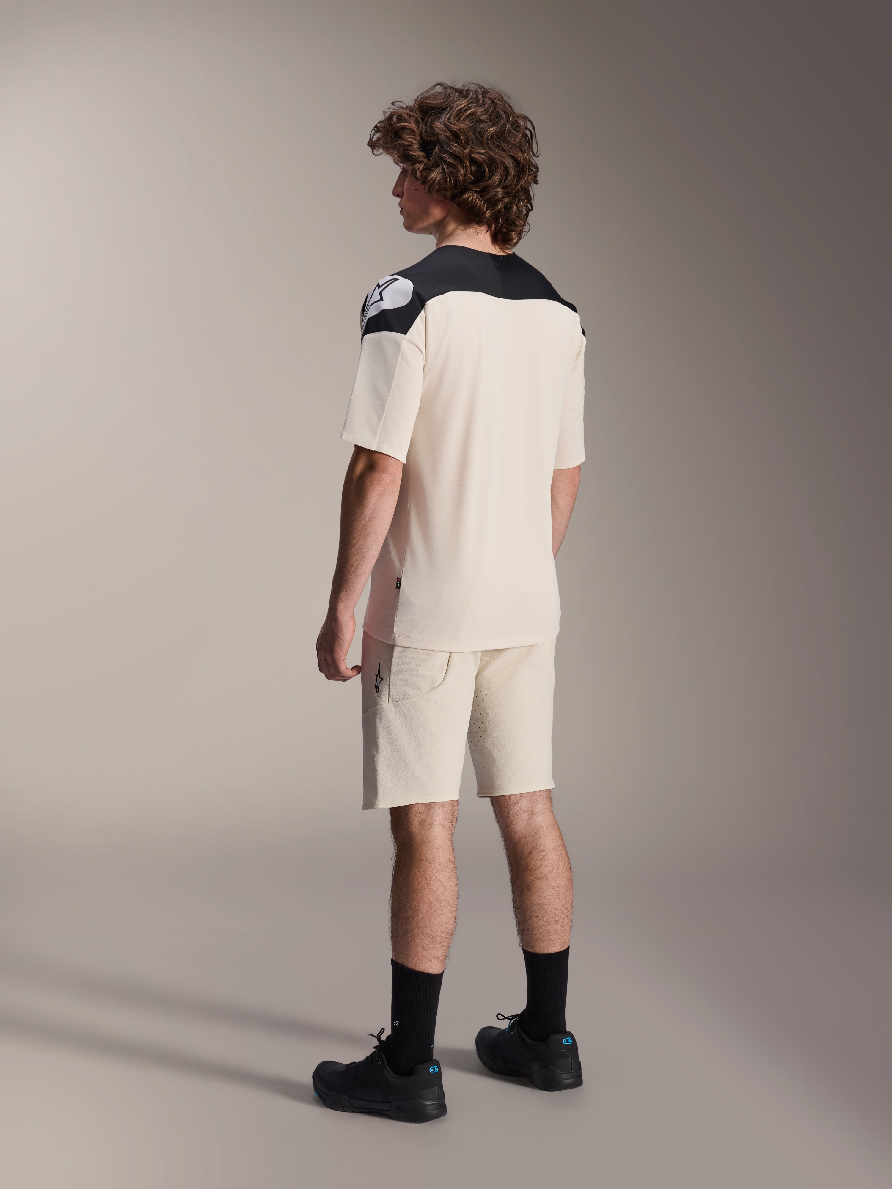 Alpinestars A-Aria Polartec Elite Short Sleeve Jersey in Ecru, maglia da mountain bike a maniche corte vista da dietro, con inserti neri sulle spalle e logo bianco, abbinata a pantaloncini ecru coordinati e scarpe nere