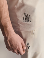 Maglia Alpinestars A-Aria Polartec Elite a maniche corte, colore Ecru, primo piano del marchio laterale con scritte 'A-ARIA', 'ALPINESTARS', 'ONE GOAL. ONE VISION.' e logo Astars, indossata con pantaloni coordinati bianco sporco, abbigliamento tecnico da MTB premium