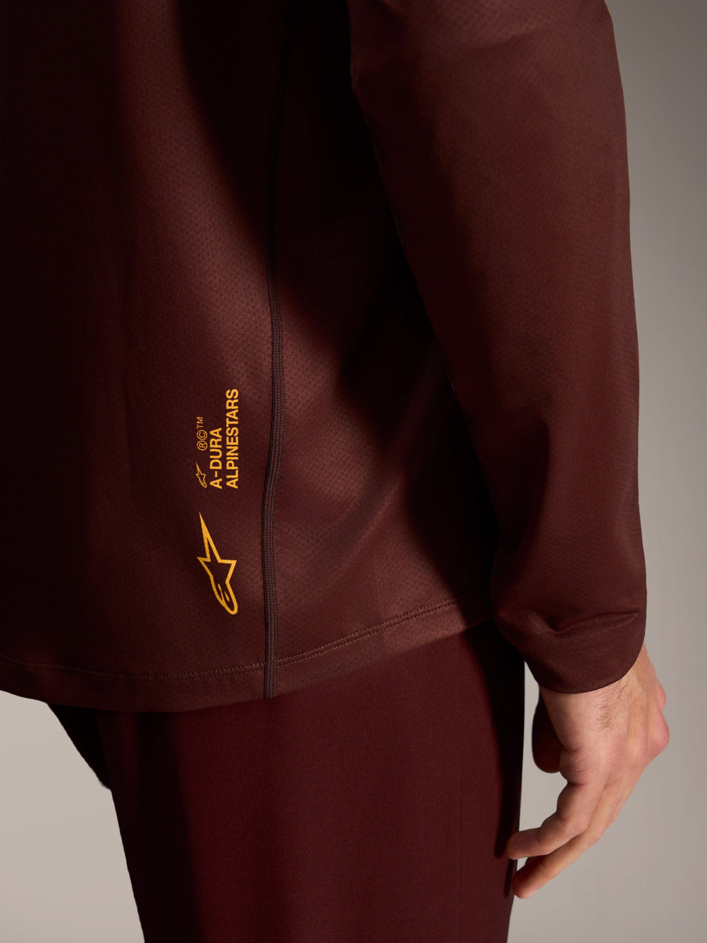 Maglia a maniche lunghe A-Dura Ride bordeaux con logo Alpinestars giallo su tessuto tecnico testurizzato.