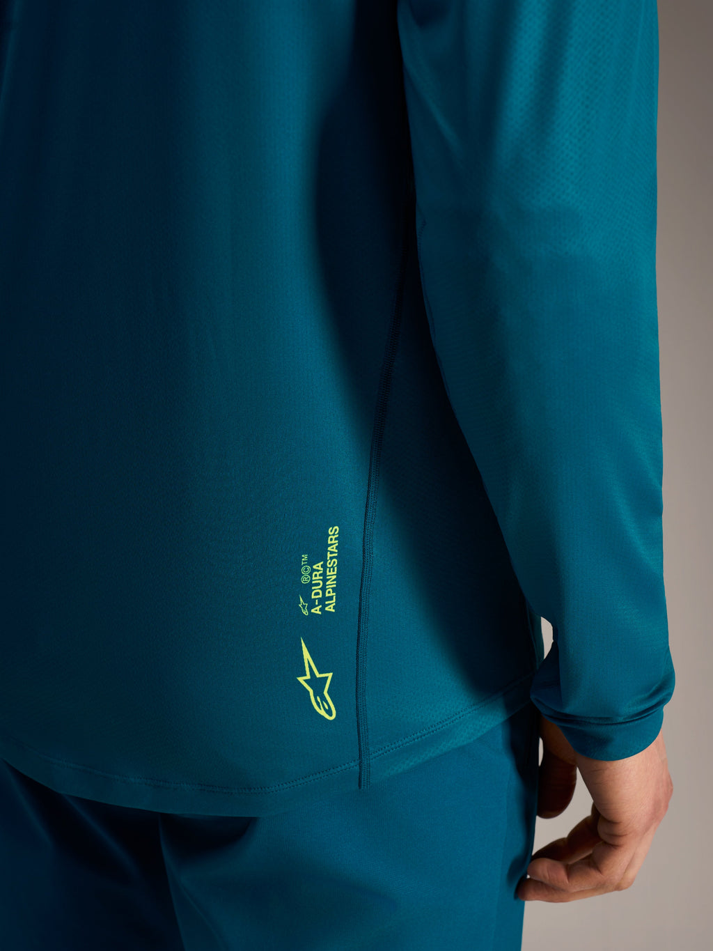 Maglia a maniche lunghe A-Dura Ride blu-verde con logo Alpinestars verde lime sul bordo posteriore testurizzato.