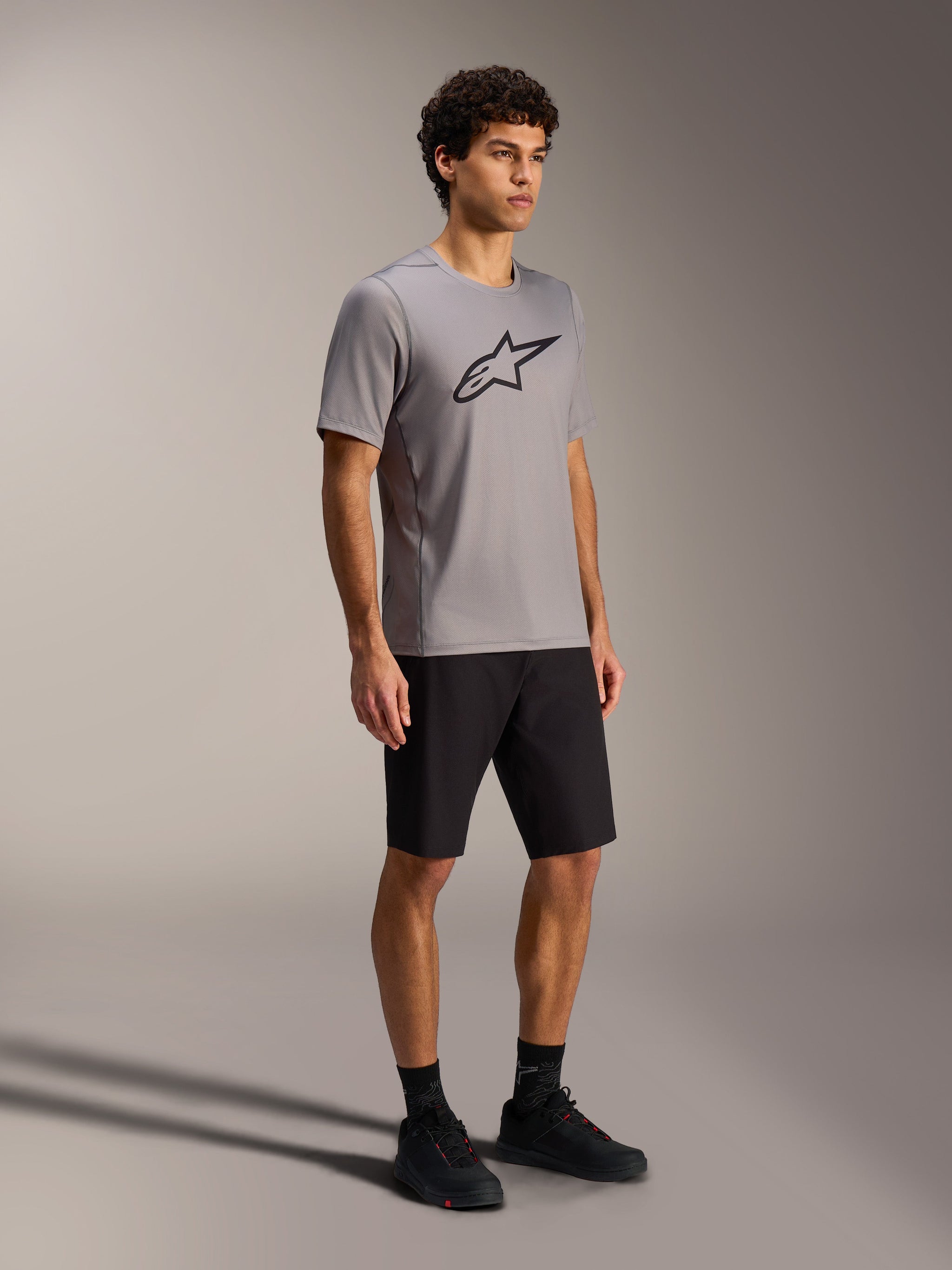 Maglia A-Dura Ride grigia a maniche corte con logo Alpinestars nero, pantaloncini e scarpe da MTB neri.