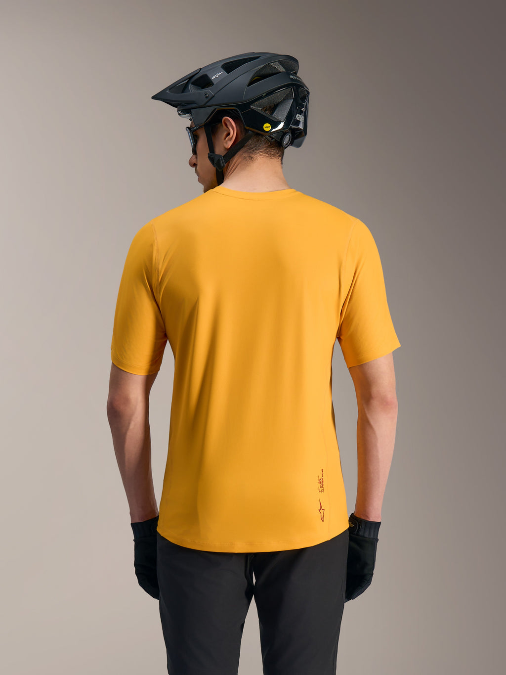 Alpinestars A-Dura Ride Jersey arancione, maglia MTB leggera con coda lunga e logo, vista dal retro con casco.