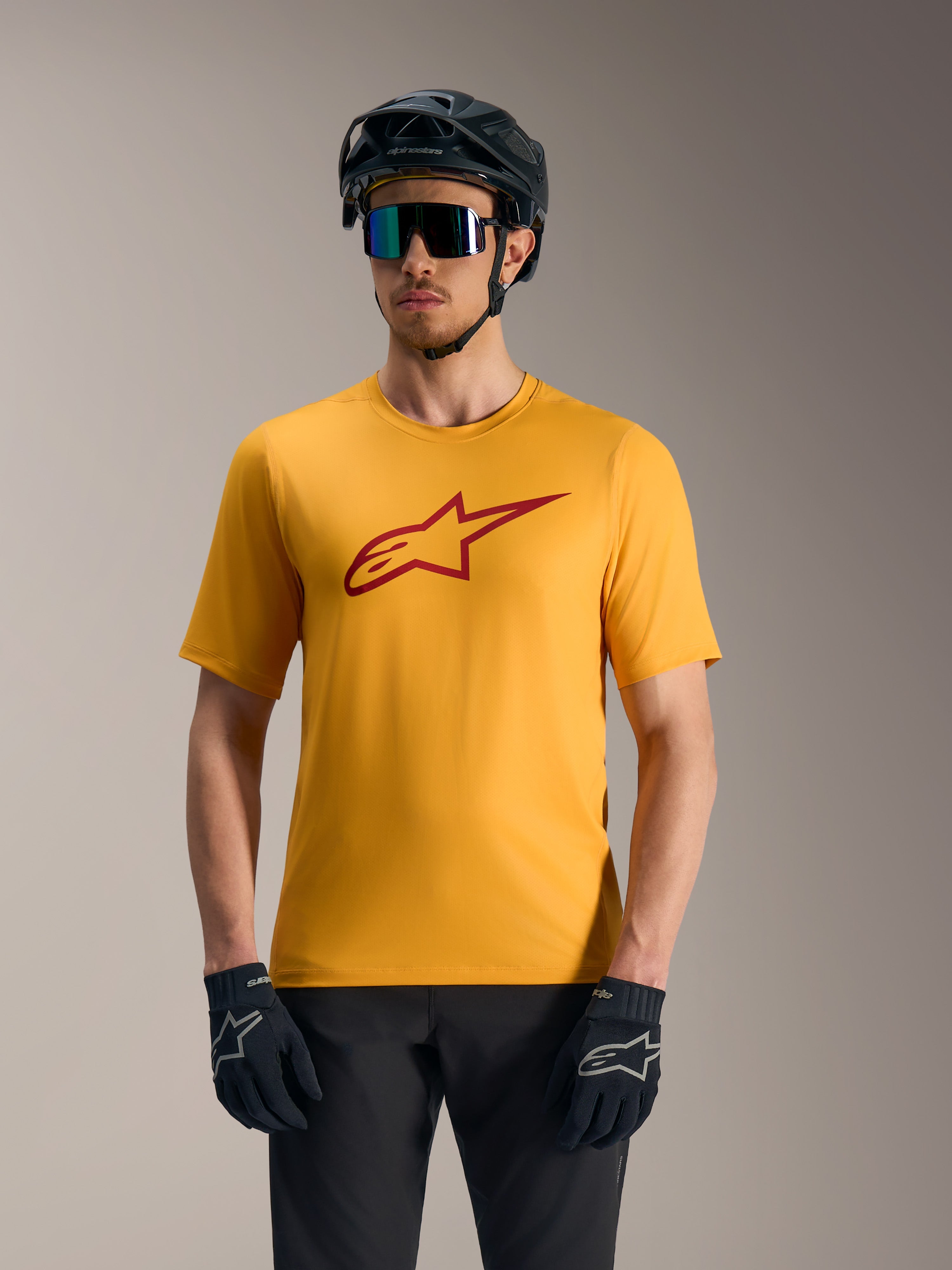Maglia A-Dura Ride arancione con logo Astars rosso, indossata con casco da mountain bike e guanti tecnici.
