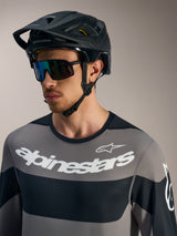 Maglia Alpinestars A-Dura Race a maniche lunghe grigia con loghi bianchi, casco da MTB nero e occhiali da sole tecnici.