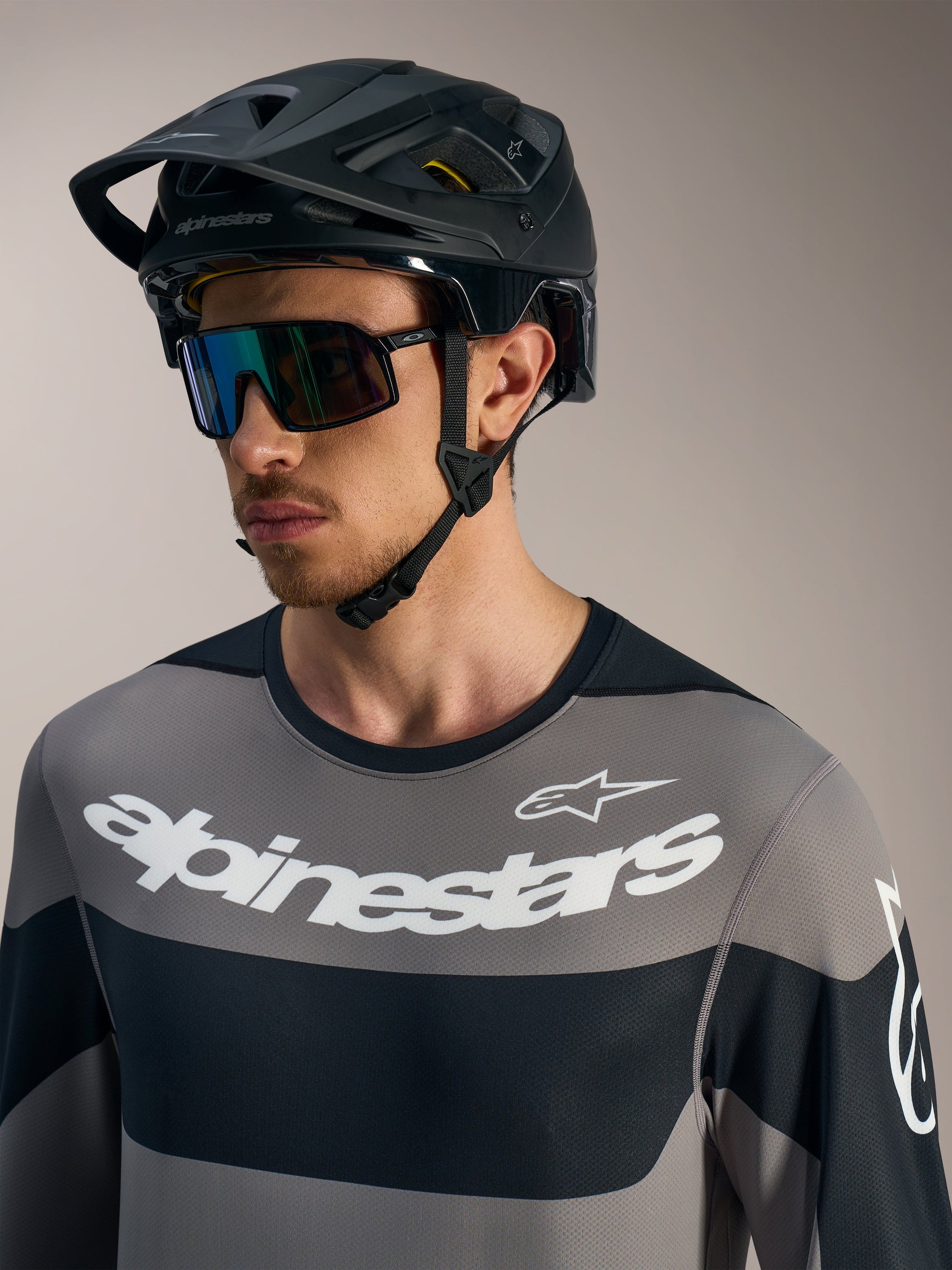 Maglia Alpinestars A-Dura Race a maniche lunghe grigia con loghi bianchi, casco da MTB nero e occhiali da sole tecnici.
