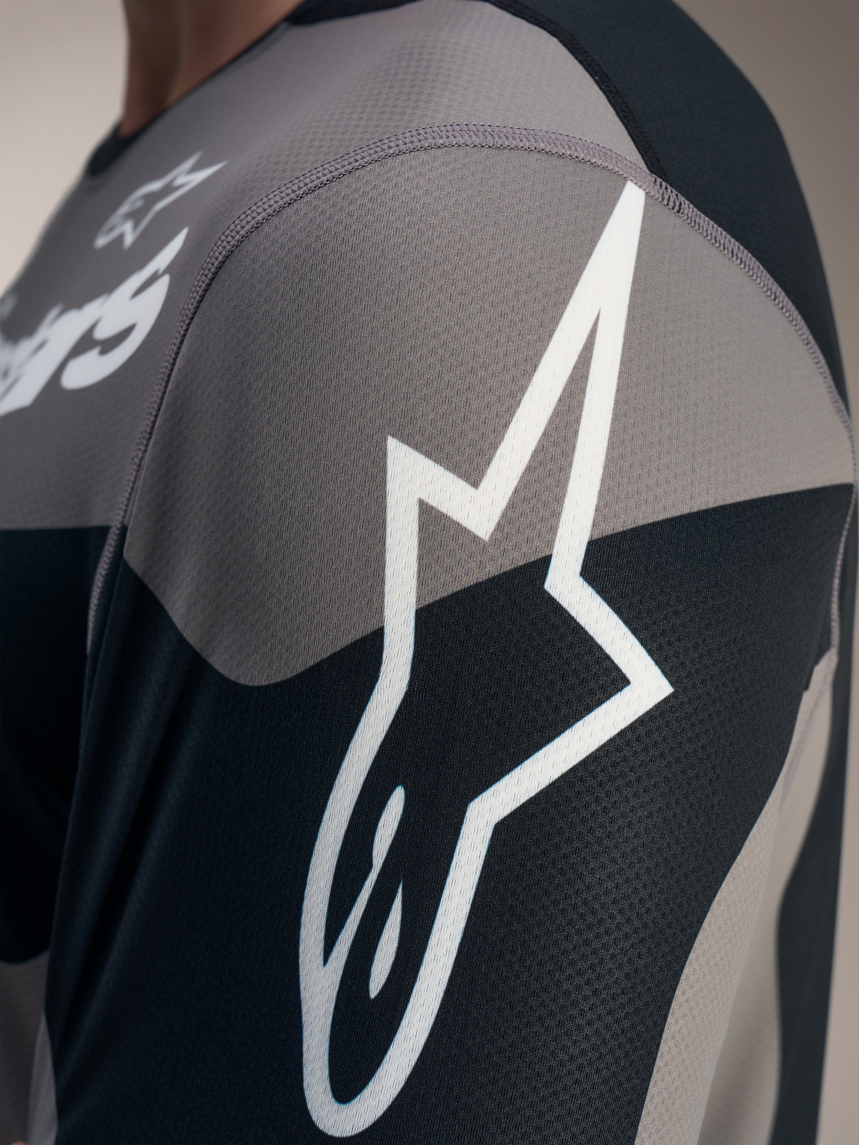 Dettaglio della maglia grigia A-Dura Race a maniche lunghe con logo Astars bianco su tessuto tecnico mesh jacquard.