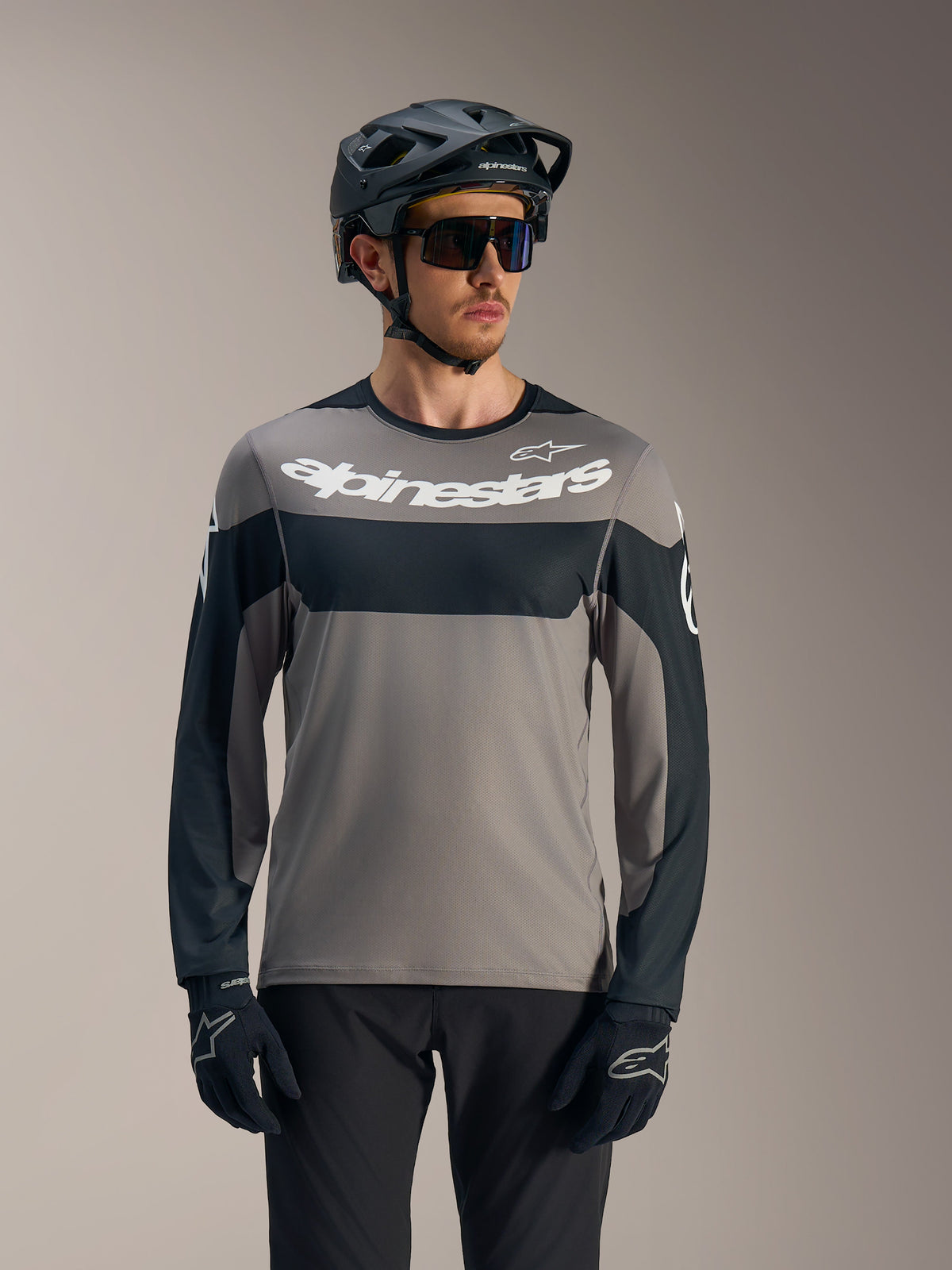 Maglia A-Dura Race a maniche lunghe grigia e nera con logo Alpinestars bianco, abbinata a casco da MTB per trail riding.