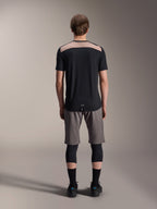 Maglia Alpinestars A-Dura Lipan - Maniche Corte, nera con pannello superiore posteriore color sabbia, vista posteriore con coda più lunga, indossata con pantaloncini MTB grigi e ginocchiere nere, abbigliamento tecnico da mountain bike