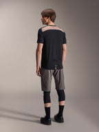 Maglia Alpinestars A-Dura Lipan a maniche corte in nero, vista posteriore su modello che mostra l'inserto in rete traforata marrone chiaro sulla parte superiore della schiena, abbinata a pantaloncini da mountain bike grigi e ginocchiere nere per un outfit completo da trail riding.