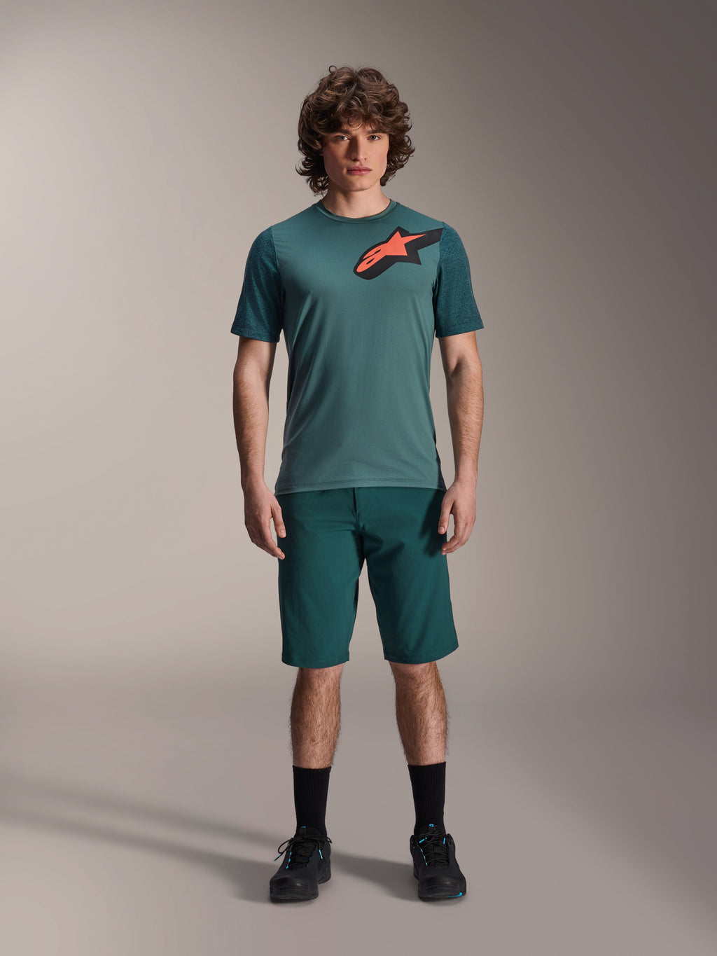 Alpinestars A-Dura Lipan Jersey, maglia da MTB a maniche corte, verde Silver Pine con logo Astars nero e arancione sul petto, abbinata a pantaloncini coordinati e scarpe nere, abbigliamento tecnico da mountain bike