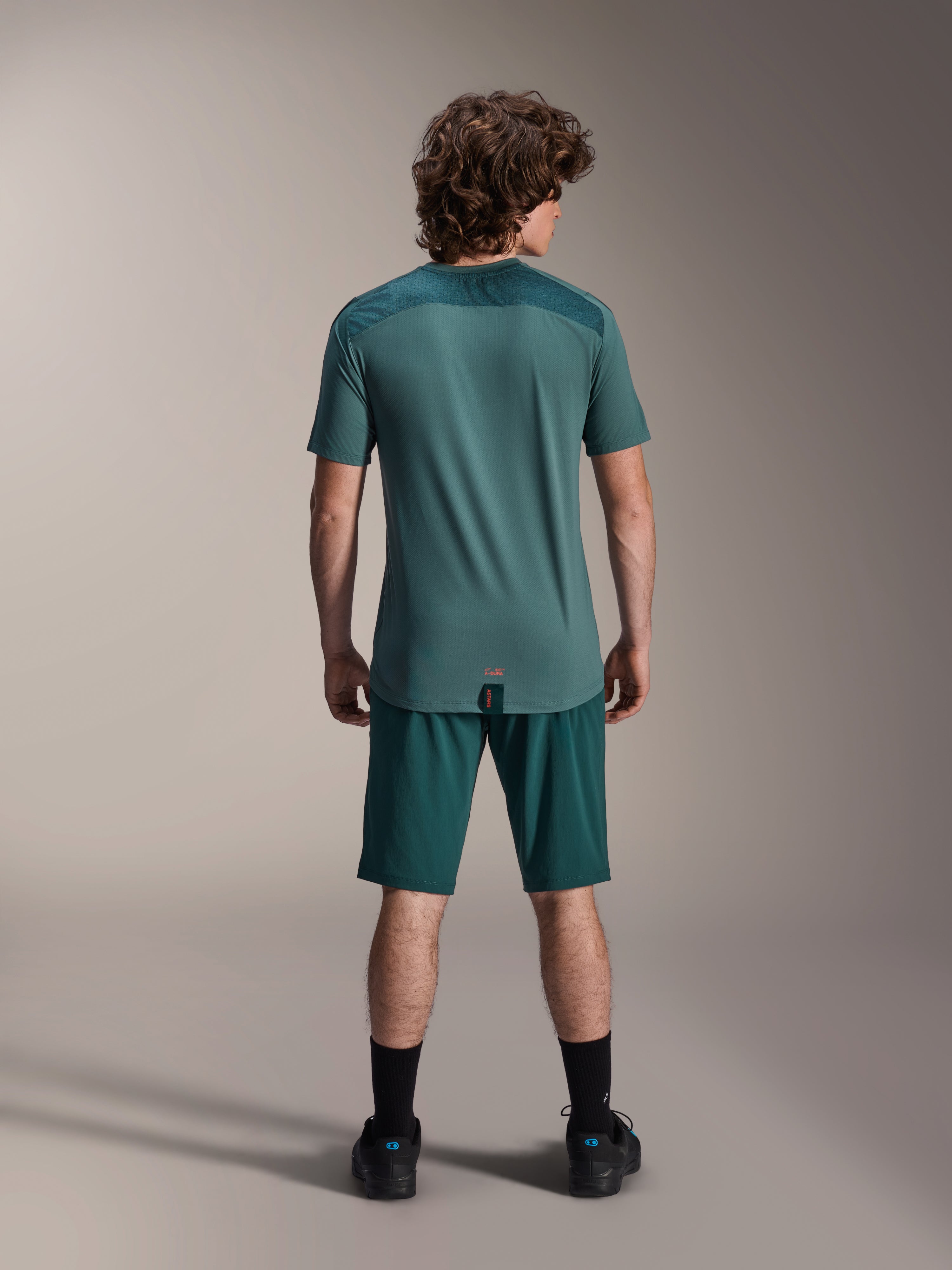 Pantaloncini Alpinestars A-Dura e Maglia A-Dura Lipan SS, verde Dark Pine, vista posteriore su un modello, abbigliamento tecnico per mountain bike con maglia a maniche corte e pantaloncini coordinati, completo da ciclismo off-road