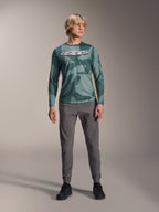 Alpinestars Maglia A-Dura Hollow Camo a maniche lunghe, Silver Pine Camo con motivo mimetico verde, grande logo "astars" bianco sul petto, indossato con pantaloni tecnici grigi e scarpe da ciclismo nere, abbigliamento MTB ad alte prestazioni