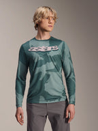 Alpinestars A-Dura Hollow Camo Jersey a maniche lunghe, maglia da MTB, motivo mimetico verde Silver Pine Camo, grande logo astars grigio chiaro sul petto, indossata con pantaloni grigi, abbigliamento da mountain bike ad alte prestazioni