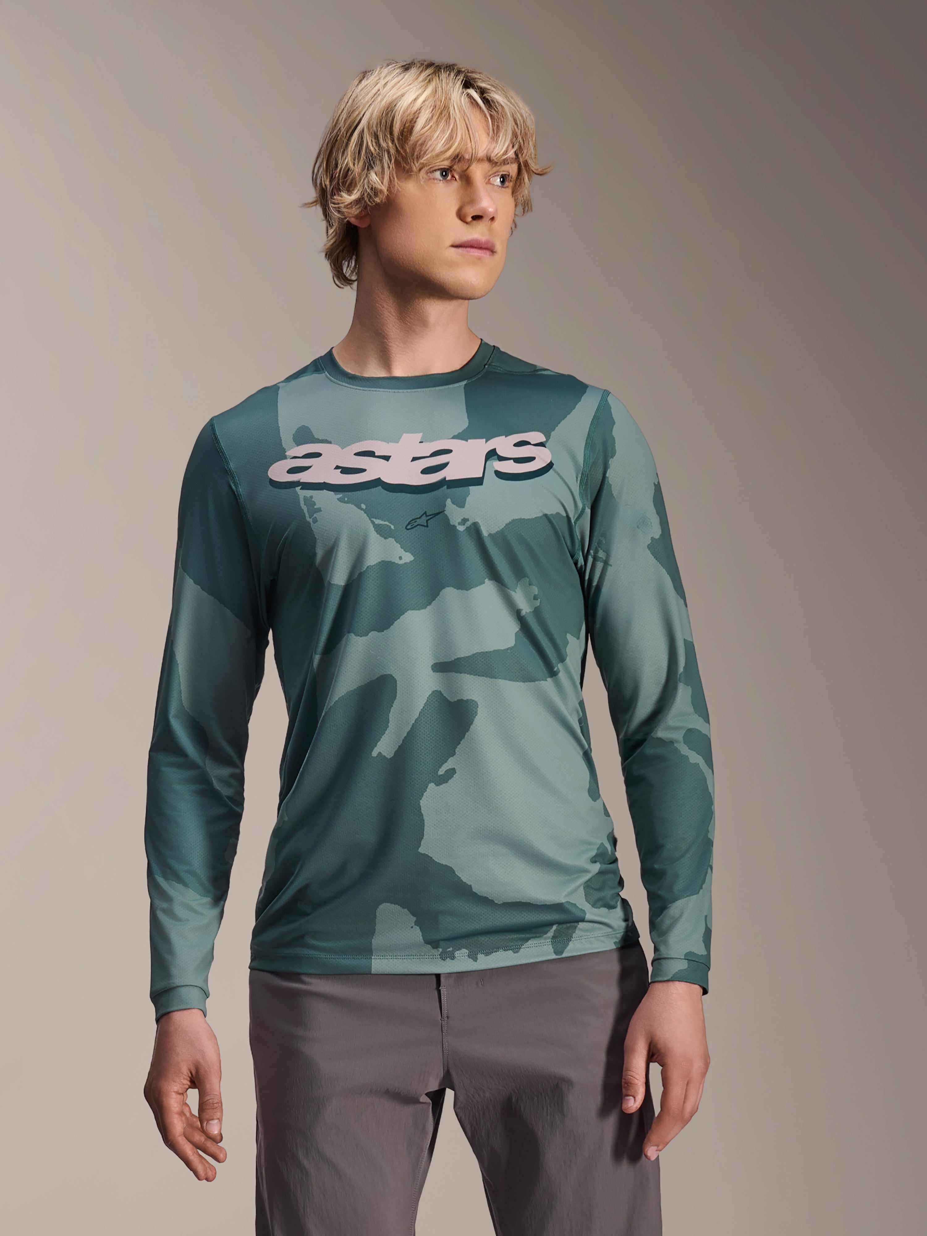Alpinestars A-Dura Hollow Camo Jersey a maniche lunghe, maglia da MTB, motivo mimetico verde Silver Pine Camo, grande logo astars grigio chiaro sul petto, indossata con pantaloni grigi, abbigliamento da mountain bike ad alte prestazioni