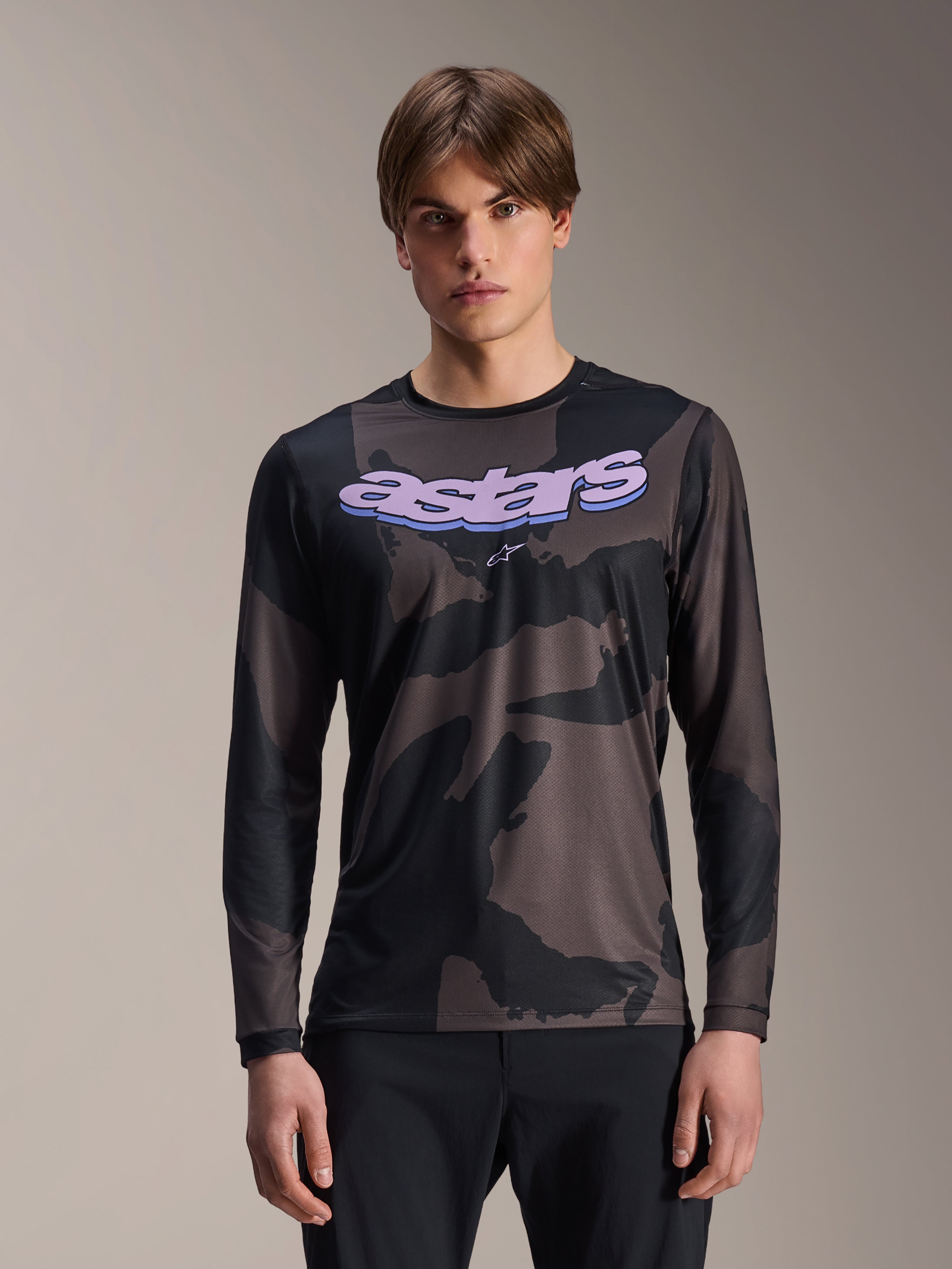Alpinestars A-Dura Hollow Camo Long Sleeve Jersey, maglia da mountain bike MTB, motivo mimetico nero e grigio, grafica 'astars' viola sul petto, indossata da un modello con pantaloni neri, design casual e performante