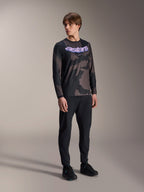 Modello che indossa la maglia a maniche lunghe Alpinestars A-Dura Hollow Camo, motivo Black Camo con grafica 'astars' viola sul petto, abbinata a pantaloni tecnici neri e scarpe nere, abbigliamento casual da MTB