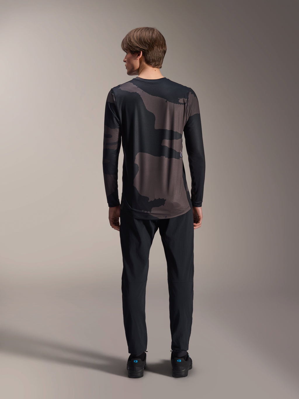 Alpinestars Maglia A-Dura Hollow Camo a maniche lunghe, Black Camo, vista posteriore indossata con pantaloni neri, motivo camouflage scuro e orlo posteriore allungato per maggiore copertura MTB