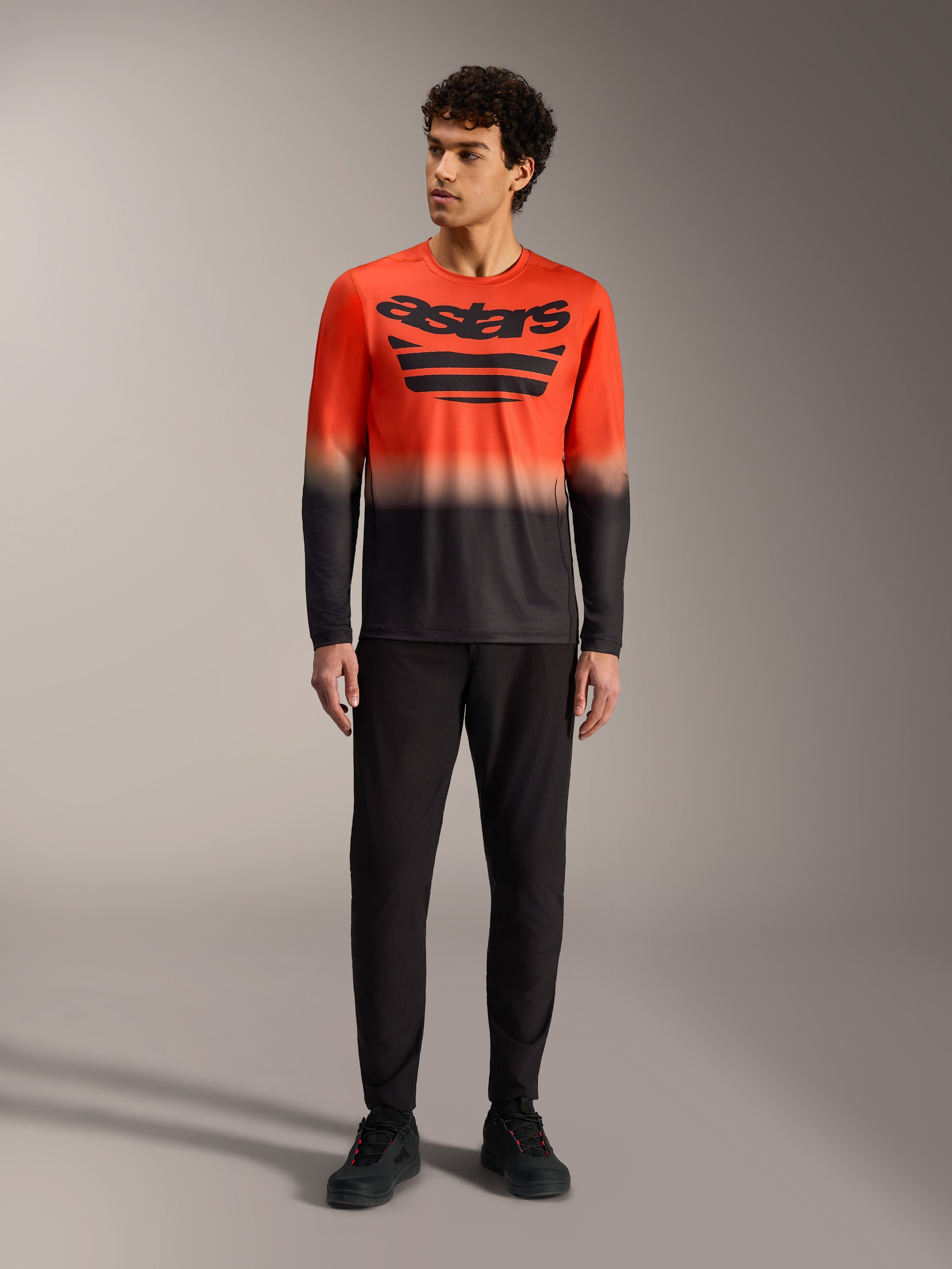 Maglia A-Dura ASTARS 2.0 arancione e nera sfumata con logo grande, abbinata a pantaloni MTB neri.
