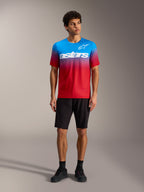 Maglia A-Dura ASTARS 2.0 con sfumatura rosso e blu, logo bianco, abbinata a pantaloncini e scarpe da MTB neri.