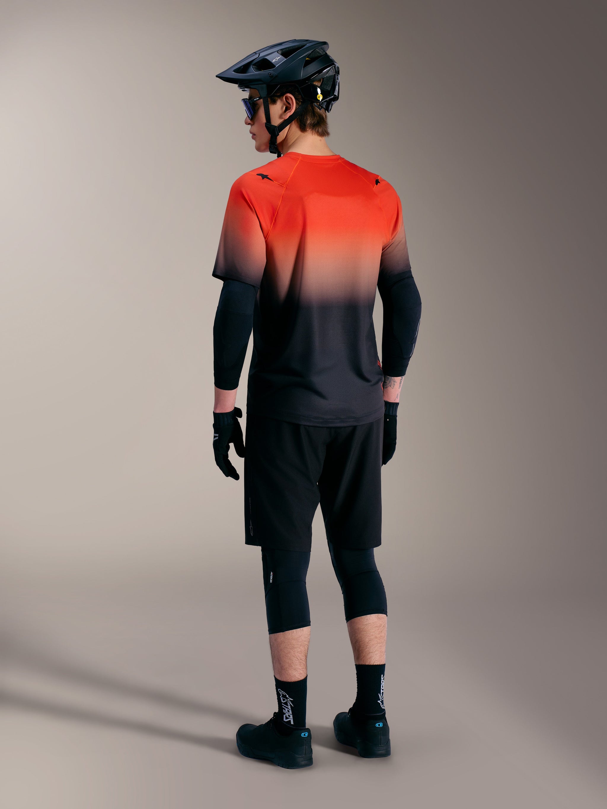 Maglia MTB A-Dura ASTARS 2.0 sfumata arancione e nero, maniche corte vista posteriore su un ciclista.