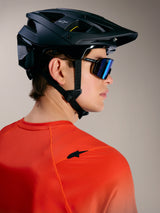 Maglia Alpinestars A-Dura ASTARS 2.0 arancione con logo nero, casco da MTB nero e occhiali da sole con lenti blu.