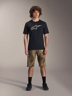 Alpinestars Maglia A-Dura Astar a maniche corte, nera con grande logo Astars bianco sul petto, indossata da un modello con pantaloncini MTB mimetici e scarpe da ciclismo nere, abbigliamento casual da mountain bike