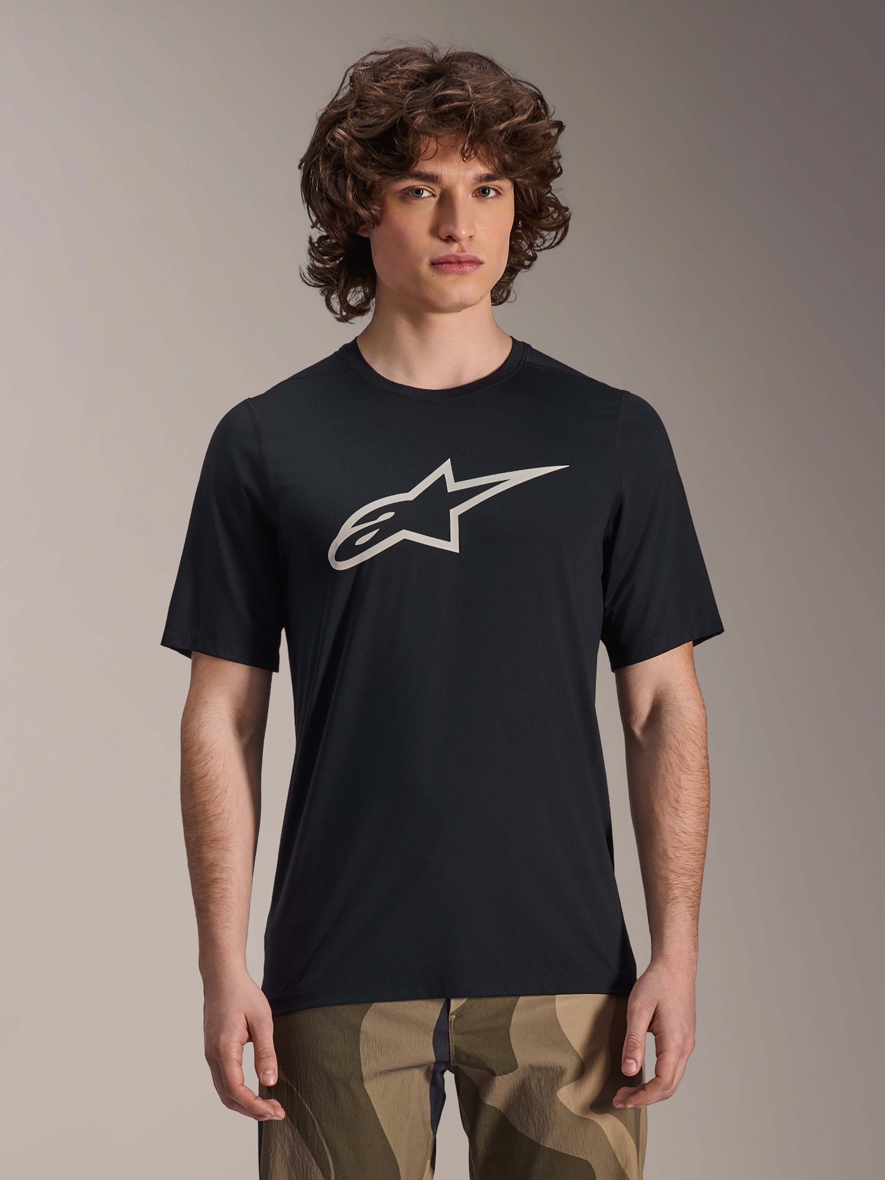 Alpinestars A-Dura Astar Jersey, maglia MTB a manica corta, nera con logo a stella bianco, indossata con pantaloni mimetici, abbigliamento mountain bike casual, tessuto tecnico traspirante