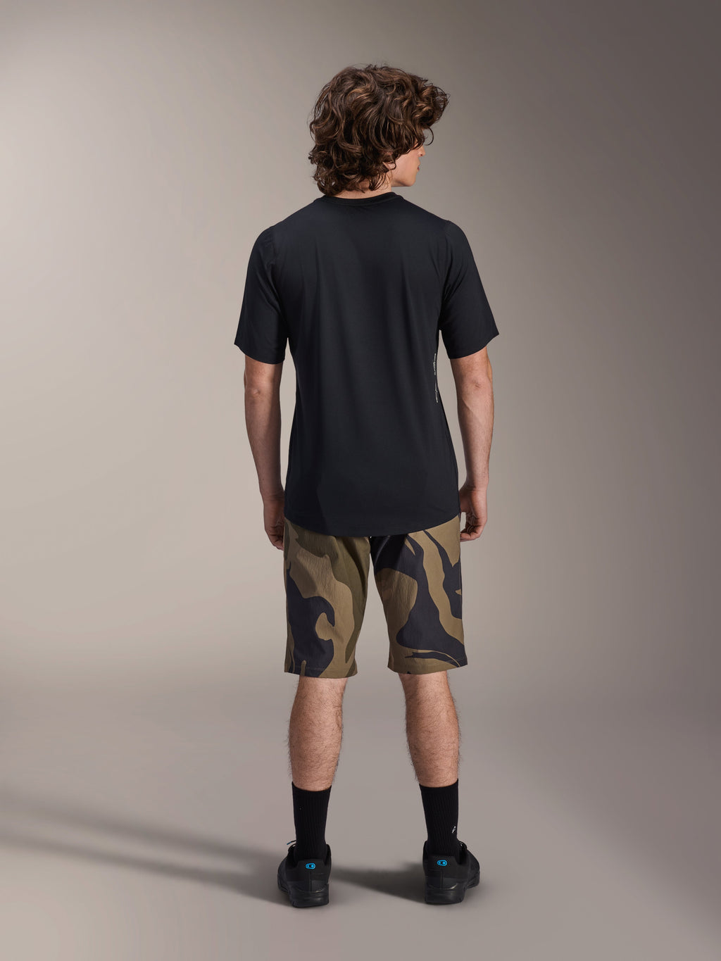 Alpinestars A-Dura Astar Maglia a Maniche Corte, nero, vista posteriore su un modello abbinata a pantaloncini da MTB mimetici e calzature nere, abbigliamento tecnico casual da mountain bike