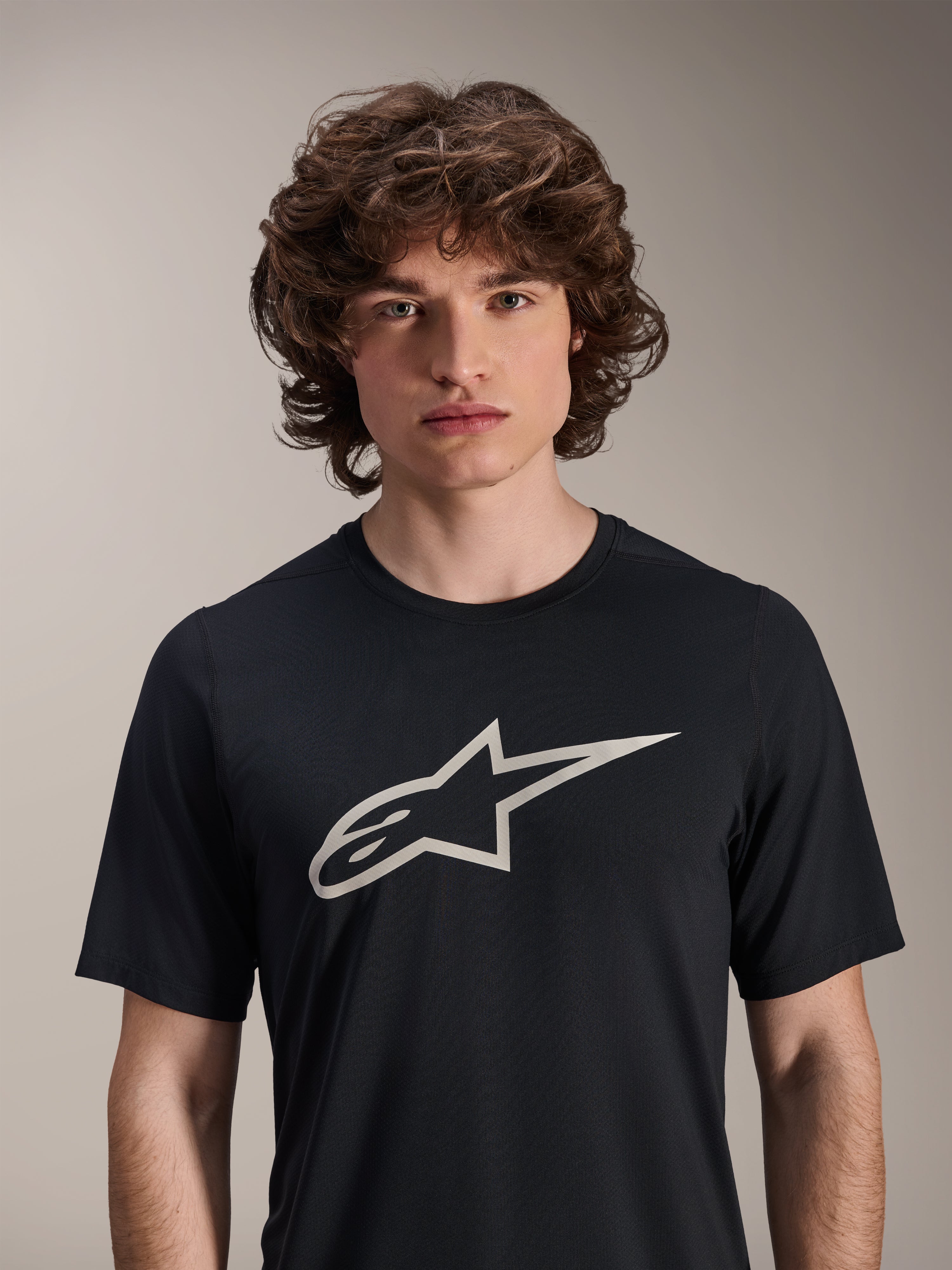 Alpinestars Maglia A-Dura Astar a maniche corte, nera, con un grande logo Astar bianco sul petto, indossata da un modello, abbigliamento tecnico casual per mountain bike