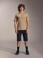 Maglia a maniche corte Alpinestars A-Dura Astar, marrone chiaro, indossata con pantaloncini neri e scarpe nere, con un grande logo Astar profilato sul petto, tessuto tecnico jacquard per il trail riding in mountain bike