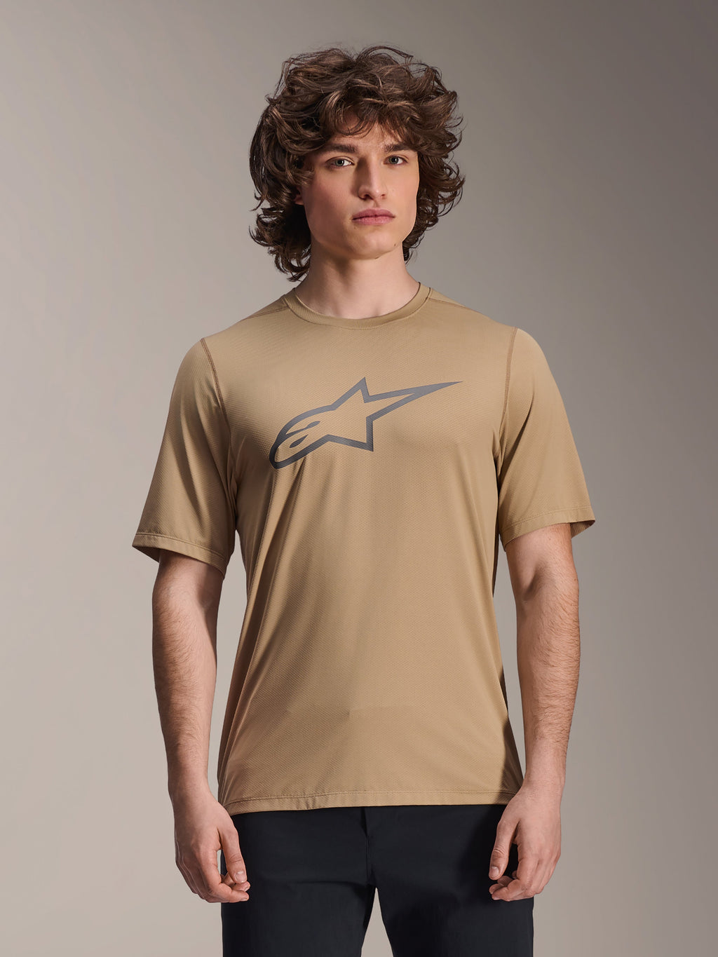 Alpinestars Maglia A-Dura Astar a maniche corte, marrone chiaro, indossata da modello uomo con pantaloni neri, logo a stella Alpinestars grigio sul petto, maglia casual da mountain bike per trail riding