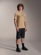 Maglia Alpinestars A-Dura Astar a maniche corte, marrone chiaro, con grande logo Astar grigio scuro sul petto, indossata da un modello con pantaloncini da MTB neri, calze e scarpe nere, abbigliamento tecnico casual da mountain bike in studio