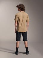 Rider visto di spalle che indossa la maglia Alpinestars A-Dura Astar a maniche corte in marrone chiaro, abbinata a pantaloncini da mountain bike neri e calze nere, stile casual per trail riding MTB