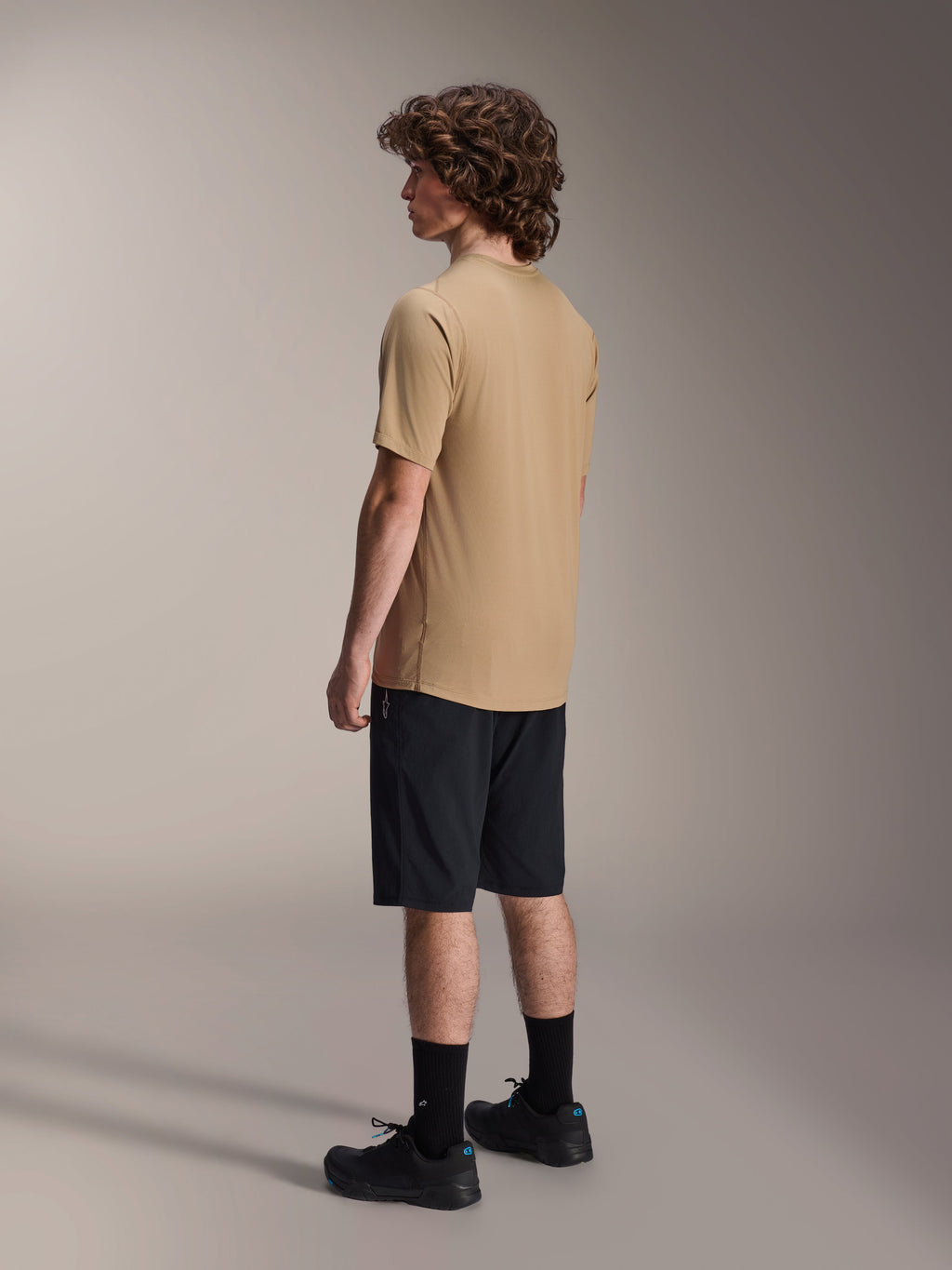 Maglia Alpinestars A-Dura Astar a maniche corte, marrone chiaro, indossata con pantaloncini neri e calze nere, tessuto jacquard traspirante, abbigliamento casual performante per mountain bike