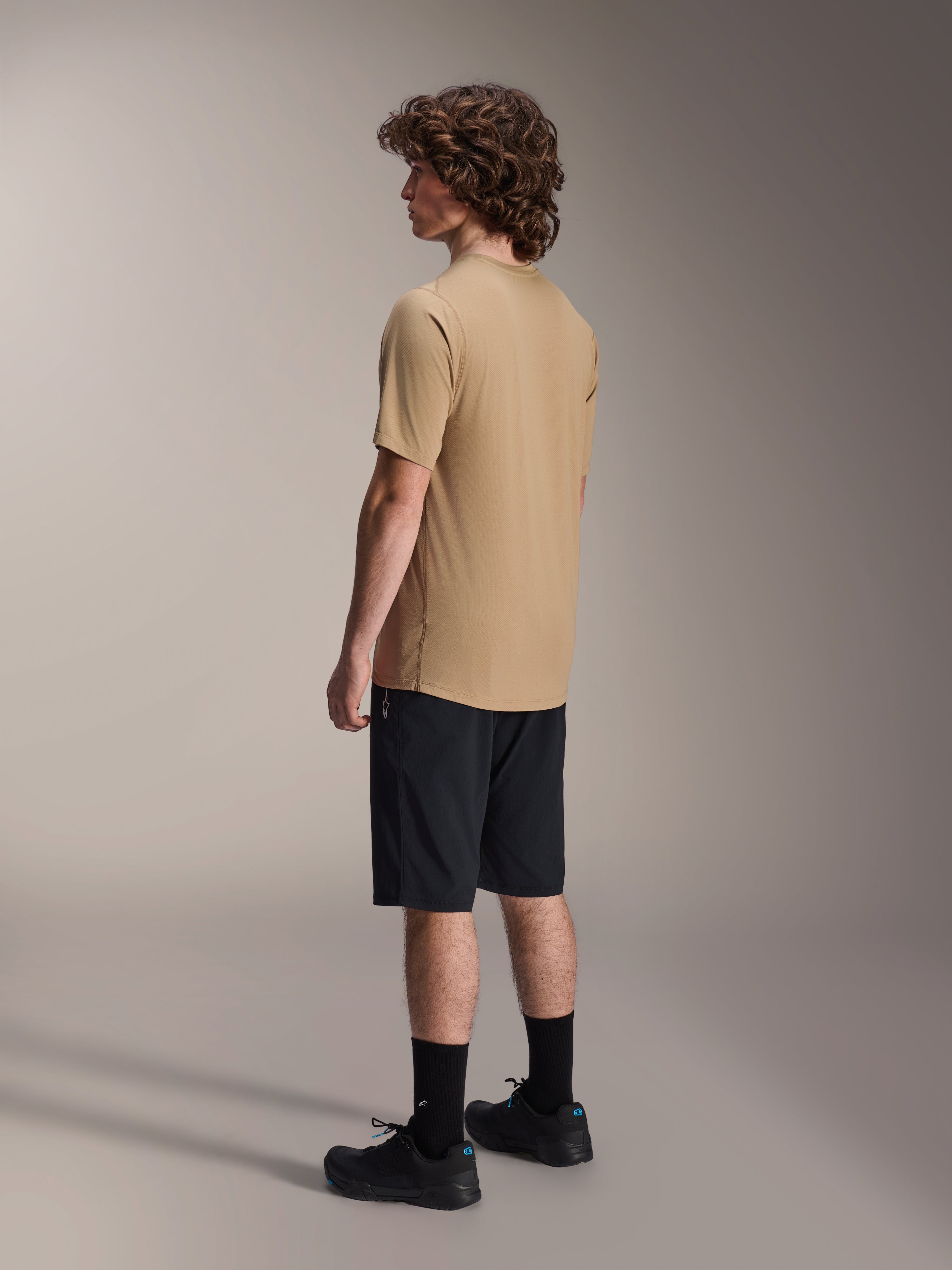 Alpinestars A-Dura Shorts, pantaloncini da mountain bike, nero, abbinati a una maglia a maniche corte A-Dura color sabbia e scarpe da ciclismo nere, con vestibilità regolare e struttura resistente per il ciclismo fuoristrada, vista posteriore laterale
