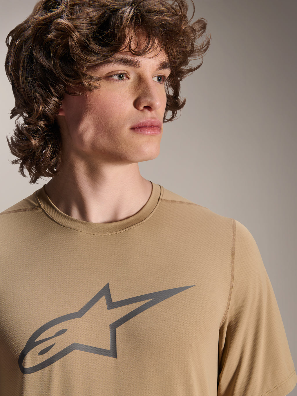 Modello che indossa la maglia a maniche corte Alpinestars A-Dura Astar, maglia da MTB marrone chiaro con logo a stella grigio sul petto, tessuto jacquard traspirante, stile casual da ciclismo