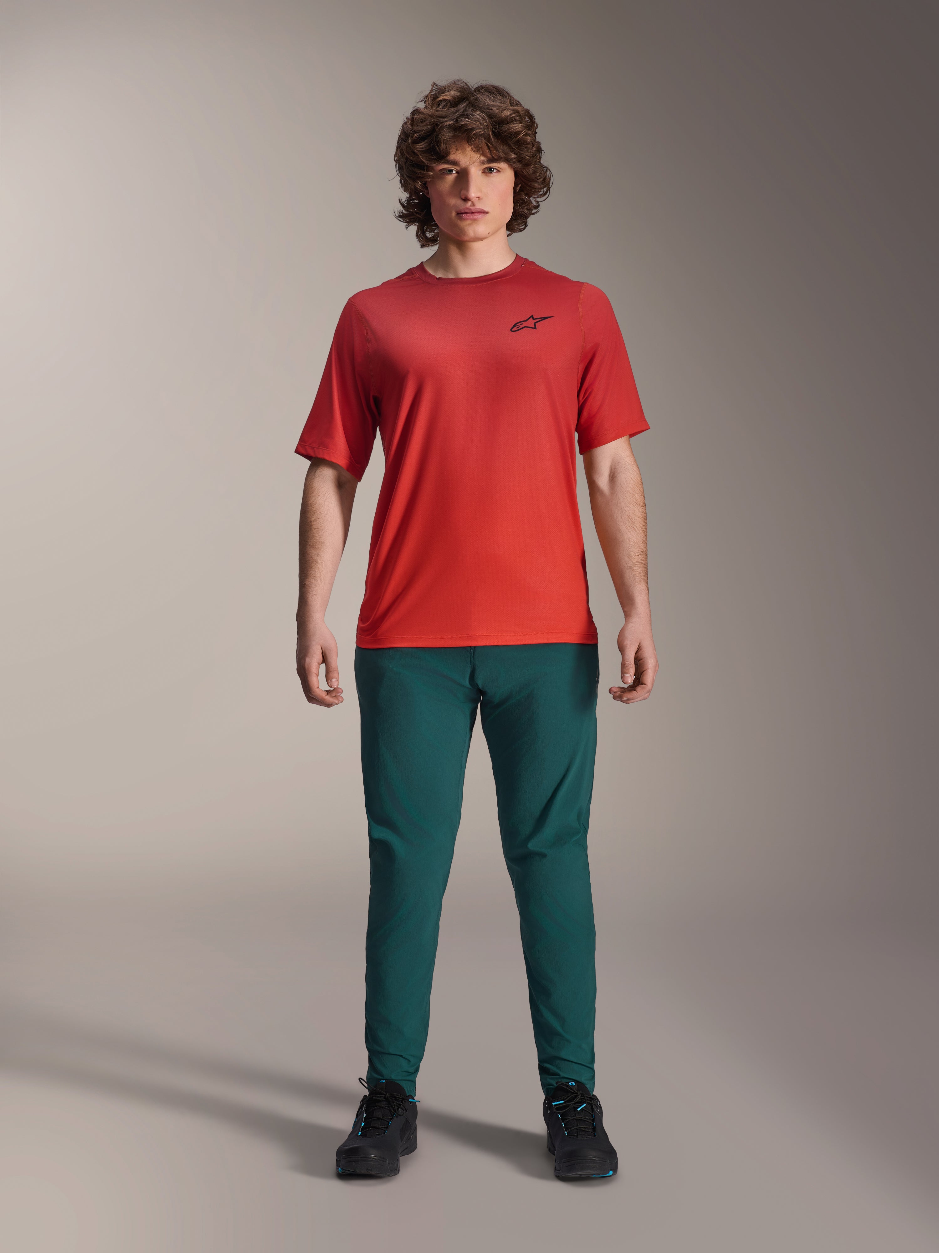 Alpinestars A-Dura Pants in verde Dark Pine abbinati a una maglia rossa A-Dura Rise a maniche corte, modello in posa con outfit completo da mountain bike, vestibilità performance casual, abbigliamento MTB resistente