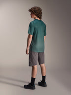 Alpinestars A-Dura Rise Jersey, maglia MTB a maniche corte, Verde Silver Pine, indossata con pantaloncini grigi e scarpe nere, vista posteriore che mostra la coda più lunga e la vestibilità regolare, tessuto leggero traspirante per trail riding