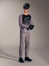 Maglia Alpinestars A-Dura Elite grigia a maniche lunghe con logo nero, abbinata a pantaloni MTB e attrezzatura tecnica.