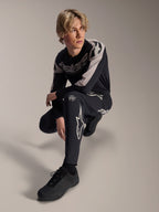 Pantaloni e maglia a maniche lunghe Alpinestars A-Supra Melt, nero e grigio, caratterizzati da audace branding bianco e loghi a stella, indossati da un modello maschile in posa accovacciata, completo coordinato da gara MTB.