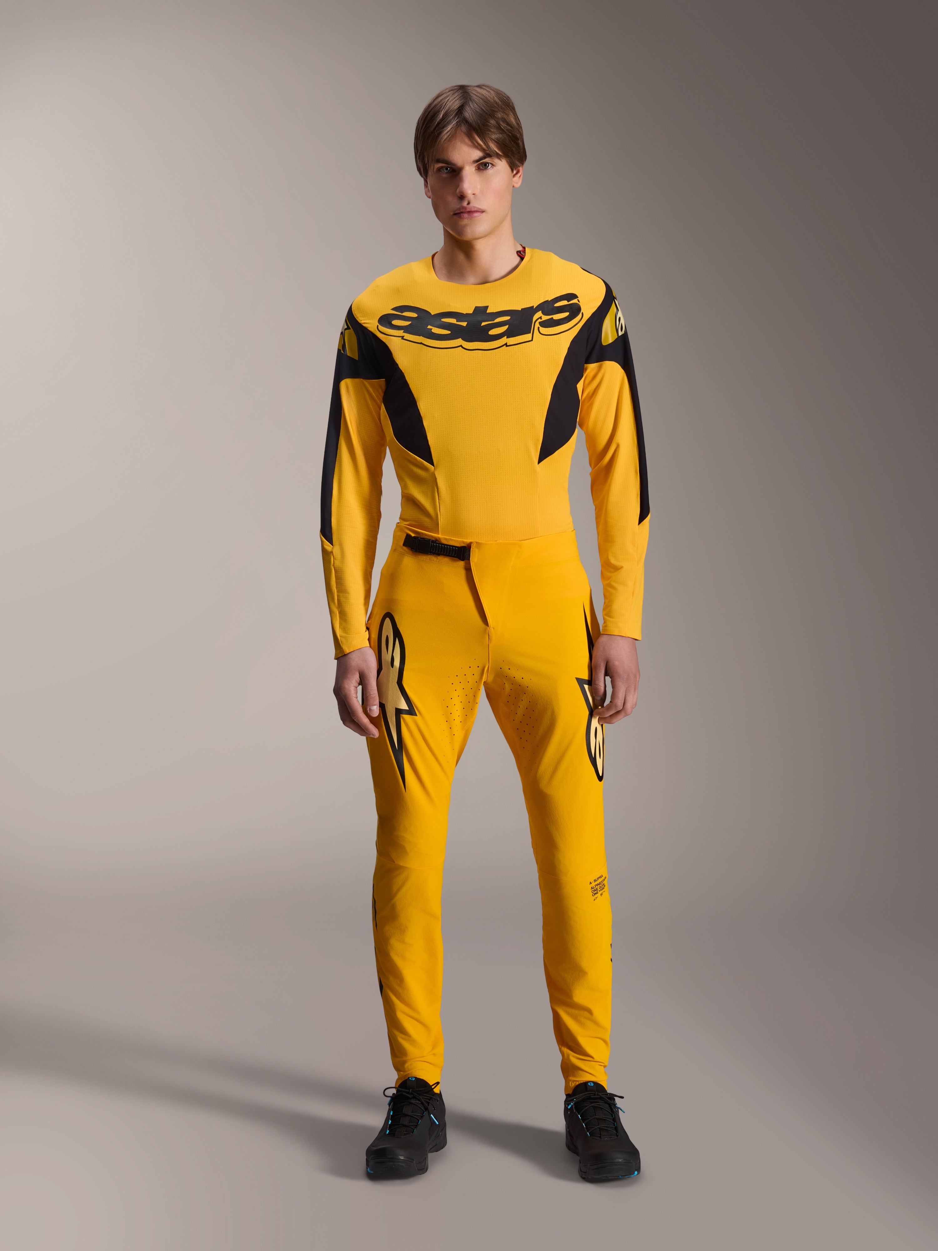 Set completo Limited Edition A-Supra Melt Gold, abbigliamento Mountain Bike Alpinestars, giallo scuro e nero, modello che indossa maglia a maniche lunghe con vistoso logo 'astars' sul petto e pantaloni tecnici coordinati, con ventilazione tagliata al laser sull'interno coscia e chiusura della vita a cricchetto, kit da gara professionale per MTB