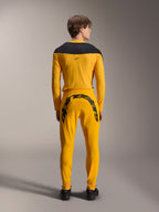 Vista posteriore di un modello che indossa il set completo Alpinestars Limited Edition A-Supra Melt Gold, composto da una maglia a maniche lunghe giallo scuro con carré nero sulle spalle e pantaloni coordinati con grande scritta Alpinestars nera sul carré posteriore, abbinato a scarpe nere.