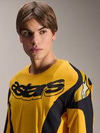 Maglia Alpinestars Limited Edition A-Supra Melt Gold, maglia da MTB a maniche lunghe, giallo scuro con grafiche nere ispirate alle corse, con scritta 'astars' nera sul petto e logo con stella sulla spalla, indossata da un modello