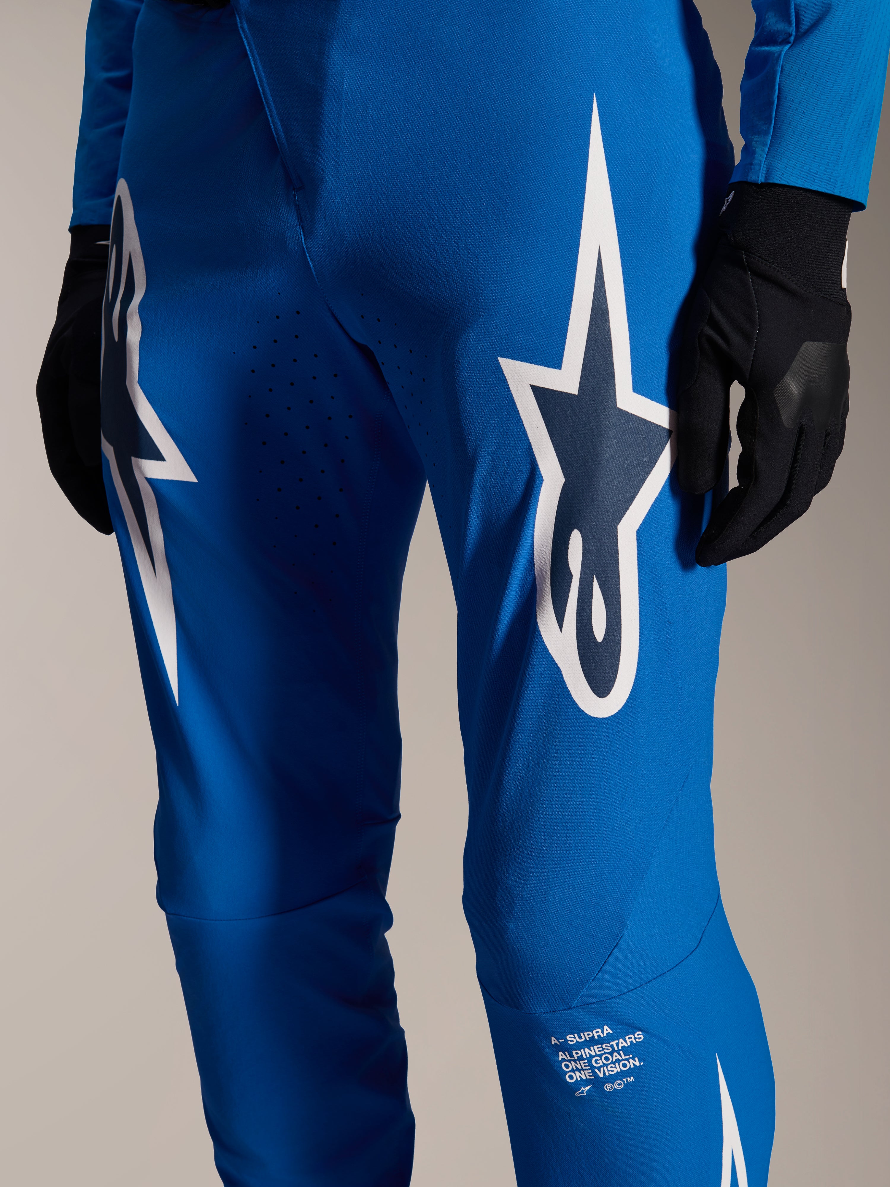 Alpinestars pantaloni A-Supra Melt, pantaloni da ciclismo blu, con grandi loghi Astars bianchi sulle cosce, perforazioni tagliate al laser per la ventilazione e branding distintivo sulla parte inferiore della gamba, indossati con guanti neri, equipaggiamento MTB performante