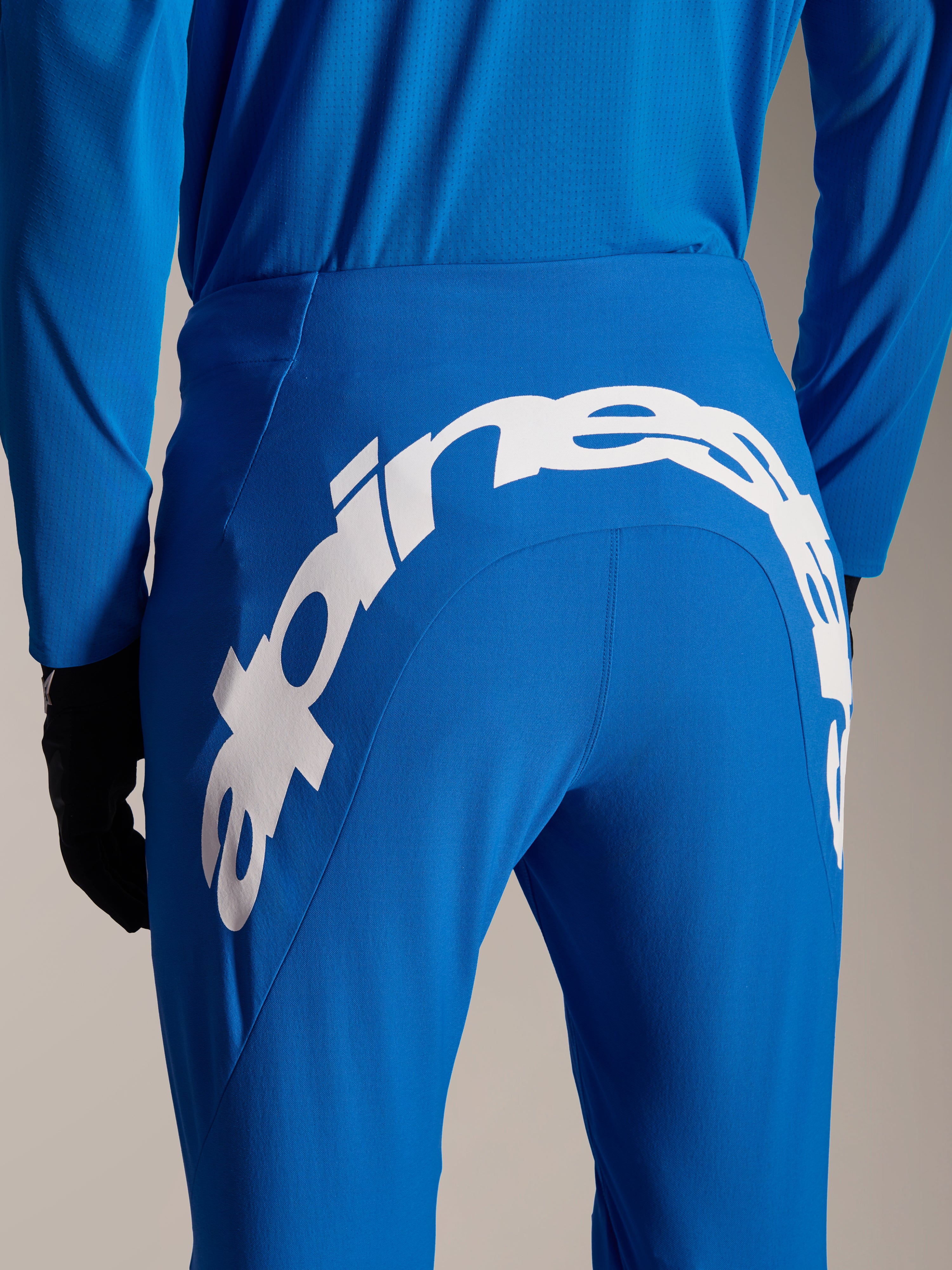 Pantaloni e maglia Alpinestars A-Supra Melt, abbigliamento MTB blu, vista posteriore con grande scritta Alpinestars bianca sul carré dei pantaloni, maglia a maniche lunghe coordinata e guanti neri