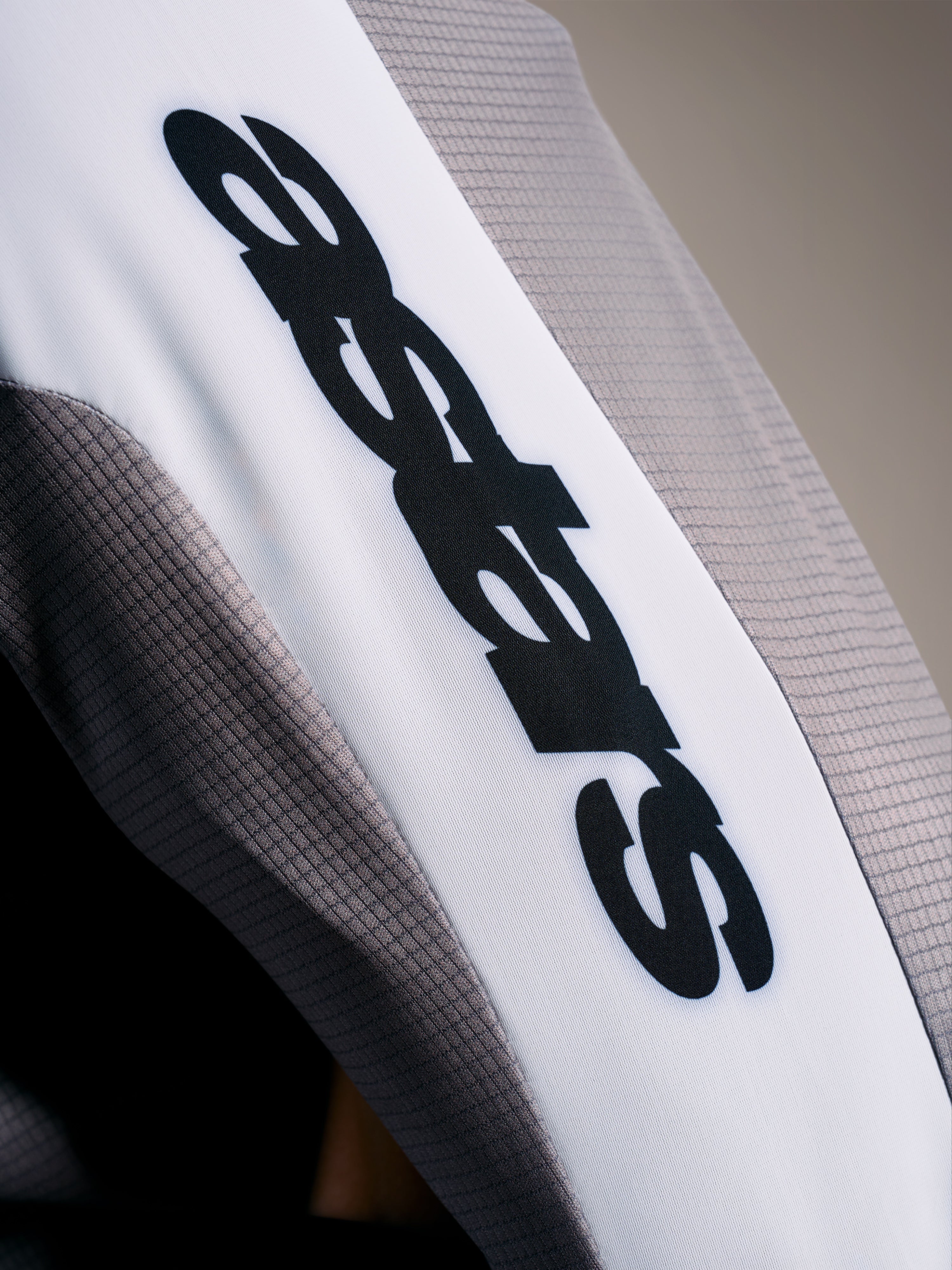 Dettaglio maglia A-Supra Elite, tessuto microforato grigio sfumato con logo ASTARS nero su banda bianca.
