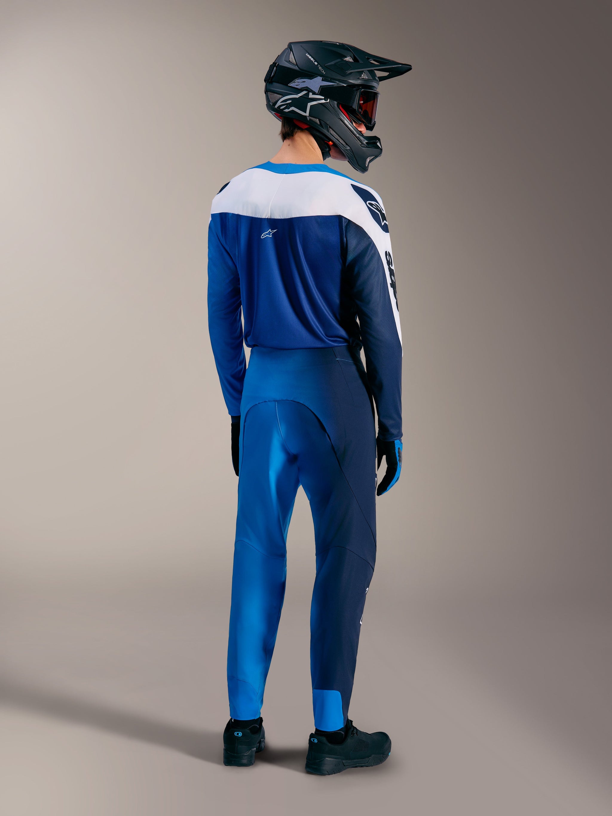 Maglia Alpinestars A-Supra Elite Faded Bright Blue, vista posteriore con kit MTB racing e casco protettivo.