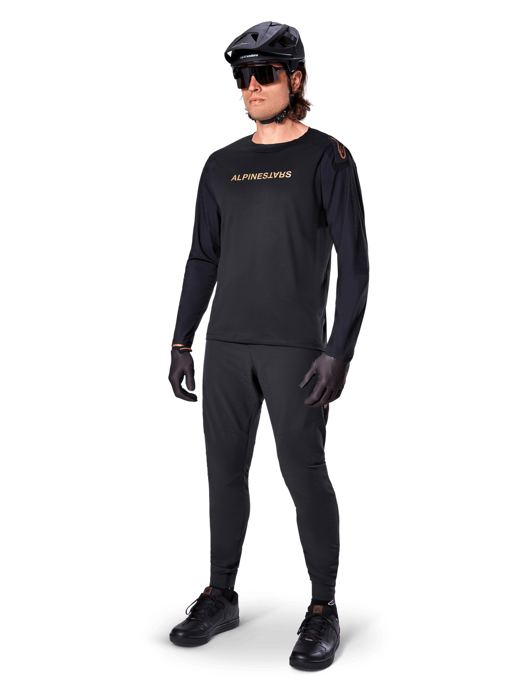 Alpinestars A-Aria Polartec Switch Jersey a maniche lunghe, nero, logo bronzo sul petto, indossata da un mountain biker con casco nero e occhiali da sole, abbigliamento tecnico da ciclismo per trail riding