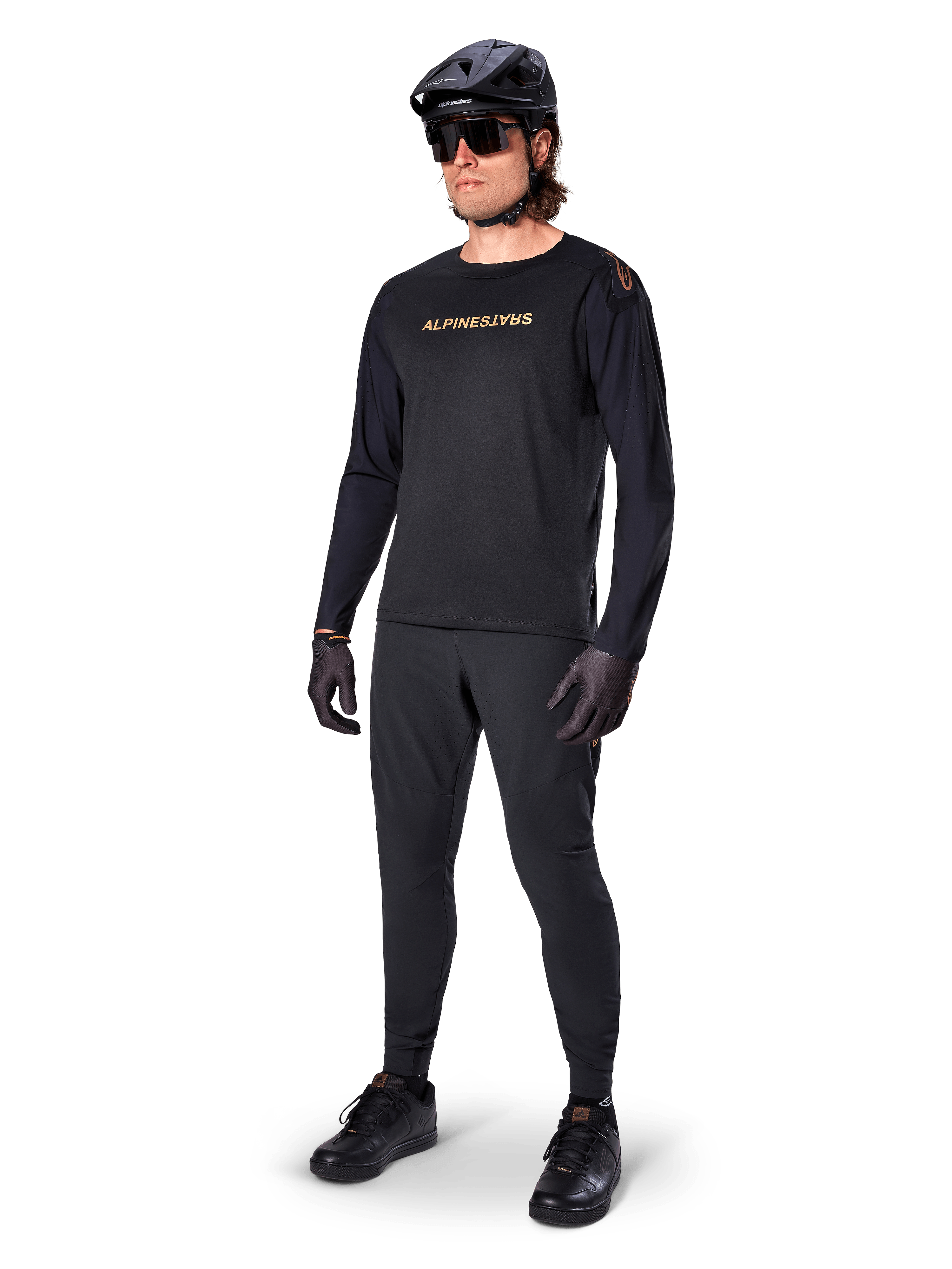 Alpinestars A-Aria Polartec Switch Jersey a maniche lunghe, nero, logo bronzo sul petto, indossata da un mountain biker con casco nero e occhiali da sole, abbigliamento tecnico da ciclismo per trail riding